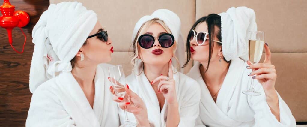 Girls Getaway Weekend in Durham 6 Celebration party at spa. Friends congratulation. Young women with champagne. Sunglasses, bathrobes and turbans on.
