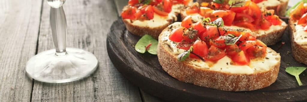 Top Spring Events in Durham 10 Bruschetta with tomatoes goat cheese and basil on a wooden table with a glass of wine. Tasty appetizer for wine.
